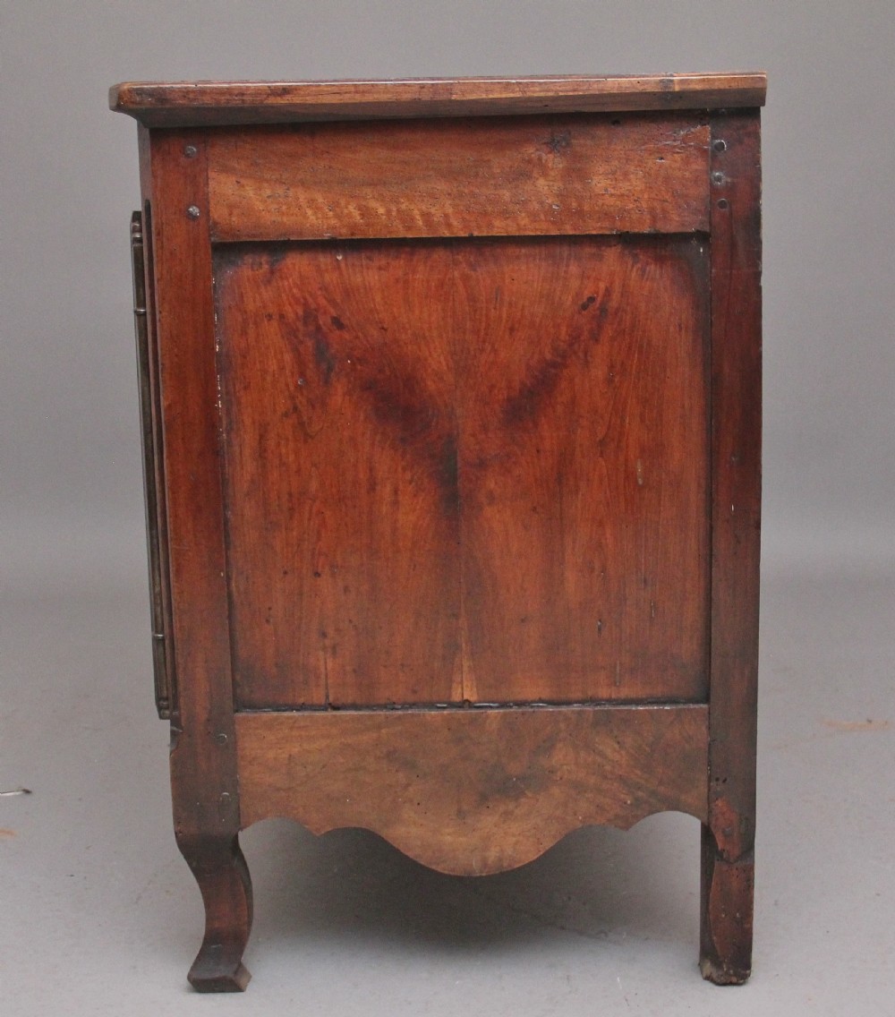 An early nineteenth-century French cherrywood dresser base featuring two cupboard doors with shaped panels, central fluting, decorative brass escutcheons, and short cabriole legs. View VII