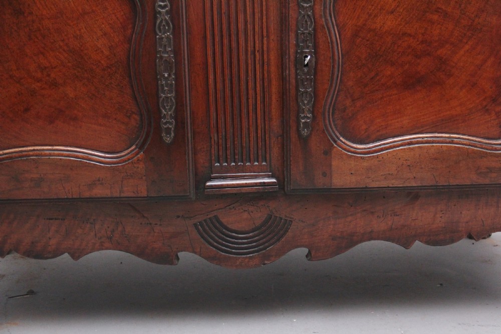 An early nineteenth-century French cherrywood dresser base featuring two cupboard doors with shaped panels, central fluting, decorative brass escutcheons, and short cabriole legs. View IX