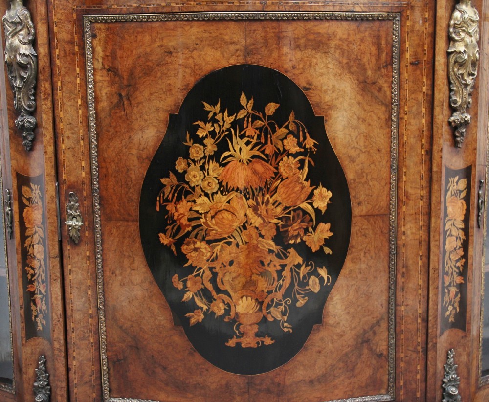 A 19th-century burr walnut credenza featuring a central door with floral marquetry inlay, flanked by two curved glazed doors and detailed ormolu mounts. View XIX