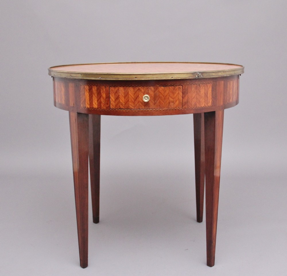 A 19th-century French oval centre table featuring kingwood parquetry, tapered square legs, a single drawer, and a brass gallery top rim.