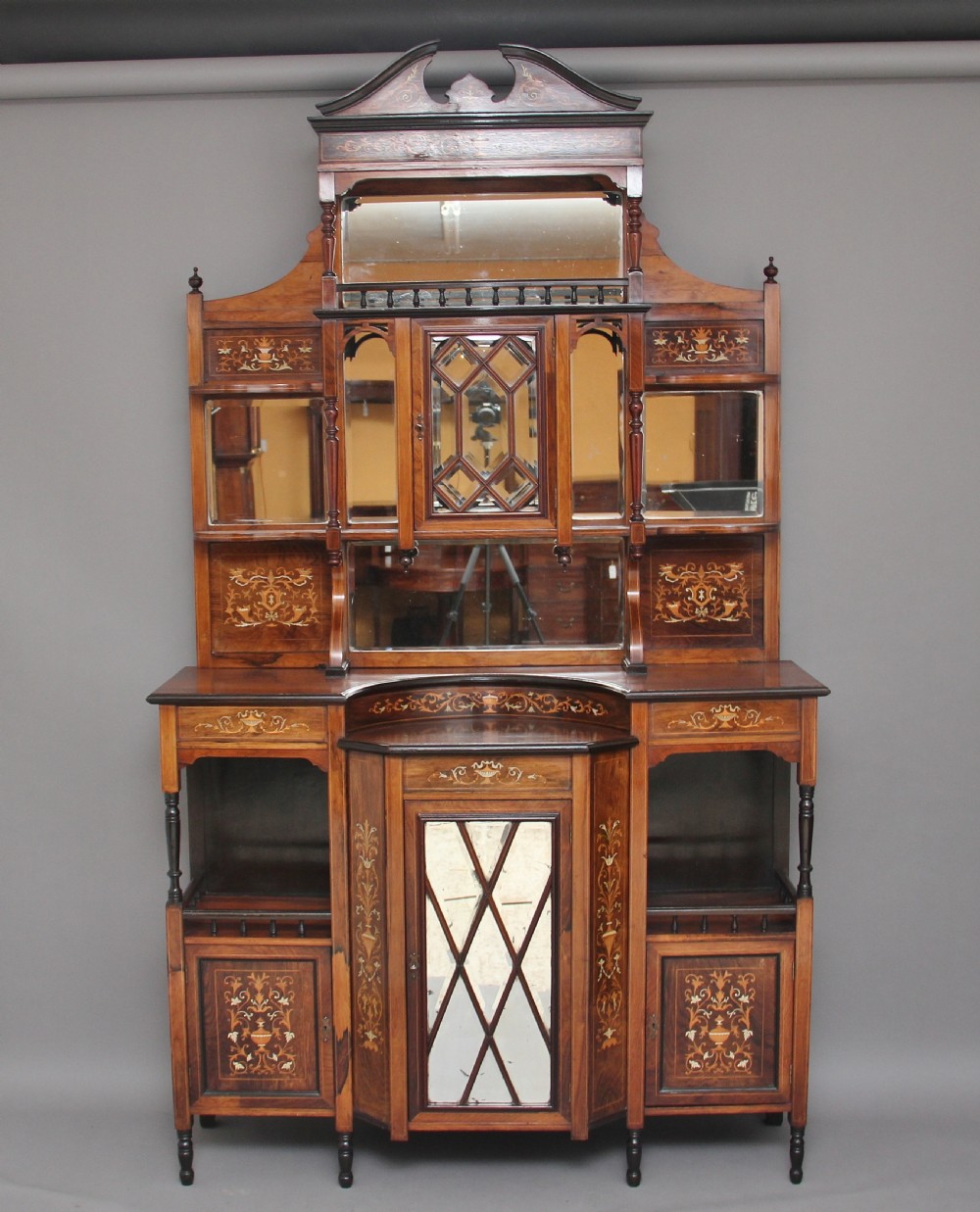 A 19th-century rosewood display cabinet featuring intricate marquetry urn inlays, mirror backs, lattice glazed doors, and a broken pediment top.