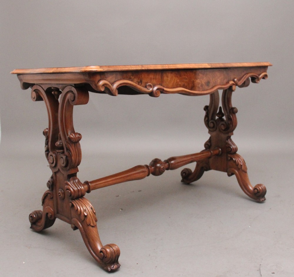 A 19th-century burr walnut centre table featuring a serpentine top and elaborate carved scroll supports joined by a turned stretcher.