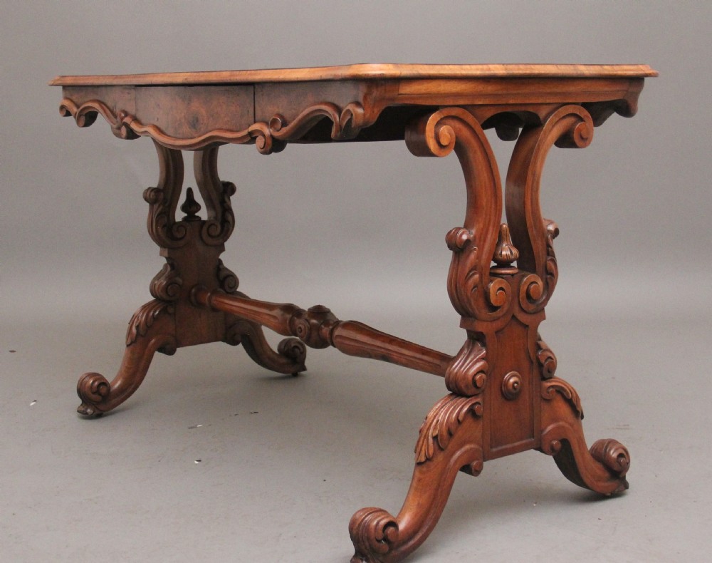 A 19th-century burr walnut centre table featuring a serpentine top and elaborate carved scroll supports joined by a turned stretcher. View V
