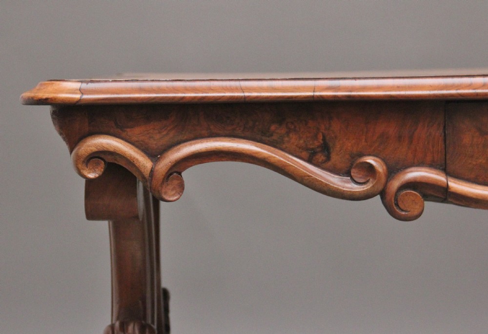 A 19th-century burr walnut centre table featuring a serpentine top and elaborate carved scroll supports joined by a turned stretcher. View XII