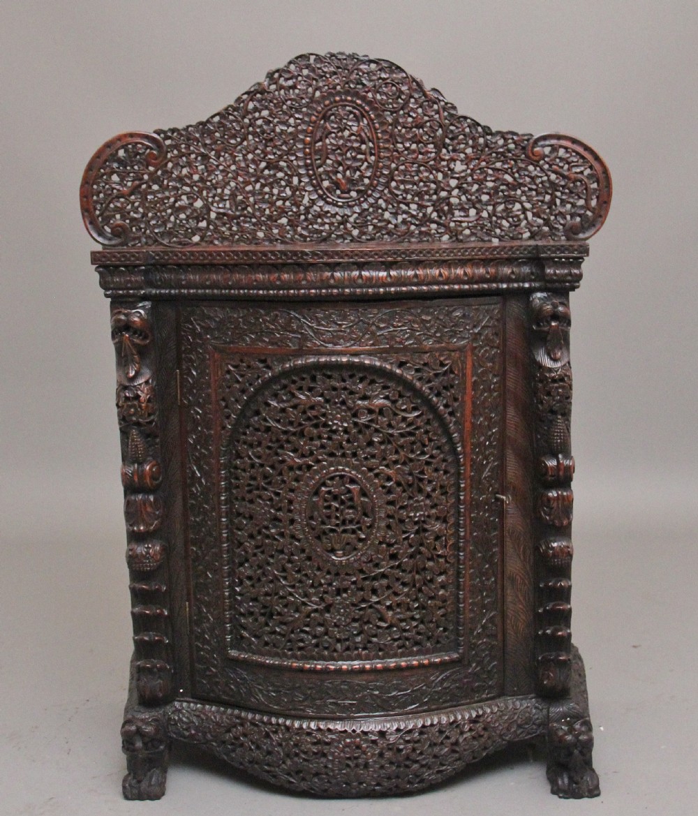 A 19th-century dark wood Anglo-Indian cabinet featuring intricate pierced floral carving, an arched panel door, and carved lion feet.