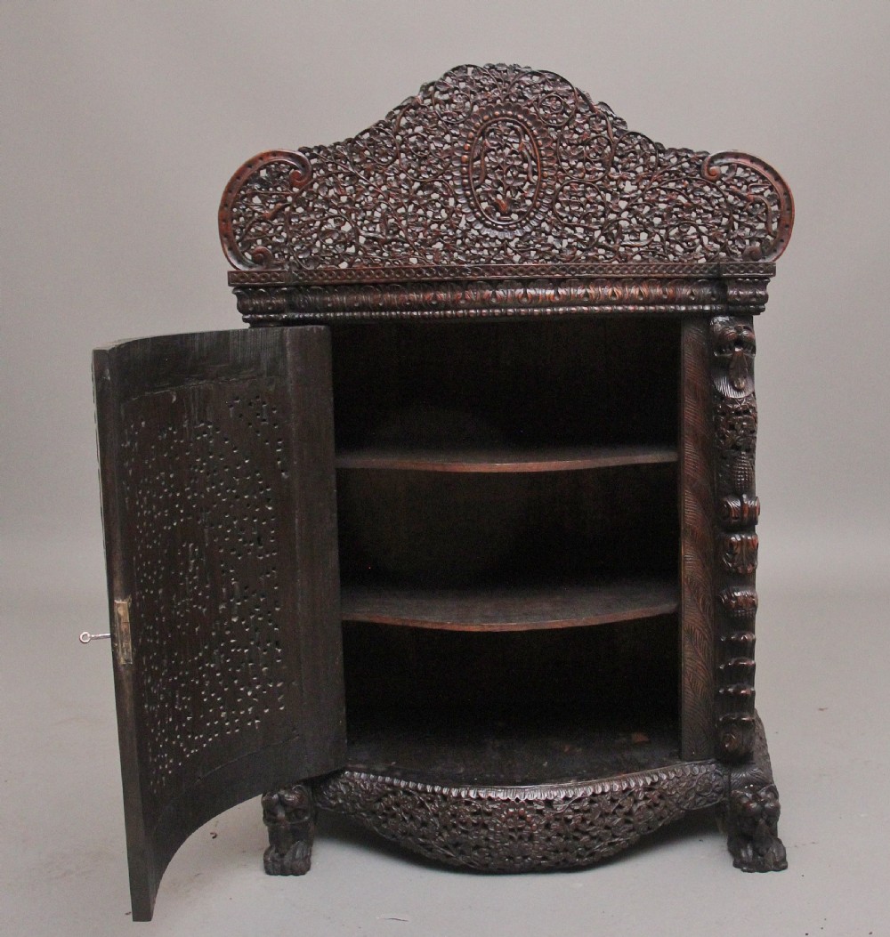 A 19th-century dark wood Anglo-Indian cabinet featuring intricate pierced floral carving, an arched panel door, and carved lion feet. View II