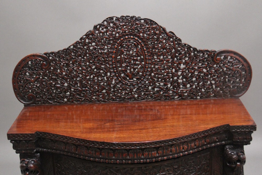 A 19th-century dark wood Anglo-Indian cabinet featuring intricate pierced floral carving, an arched panel door, and carved lion feet. View III