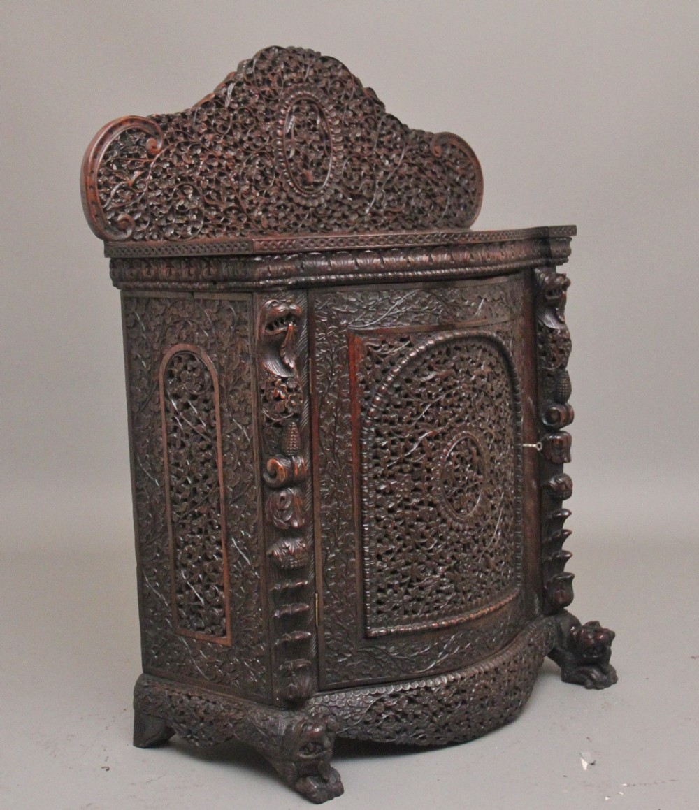 A 19th-century dark wood Anglo-Indian cabinet featuring intricate pierced floral carving, an arched panel door, and carved lion feet. View VI