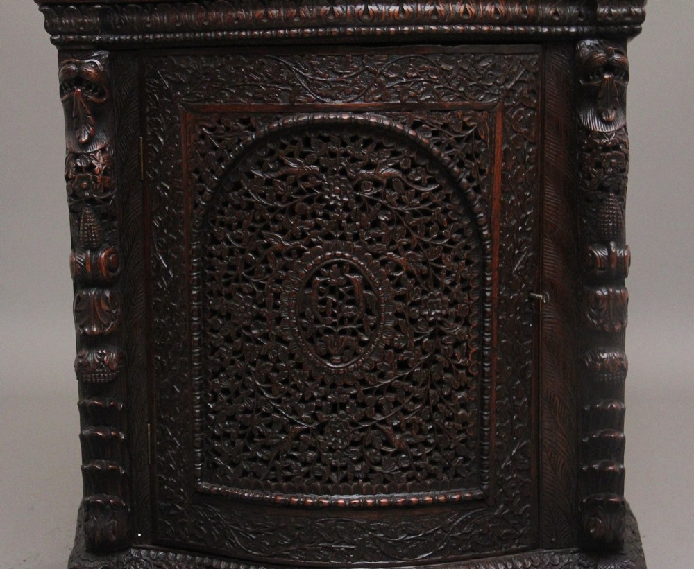 A 19th-century dark wood Anglo-Indian cabinet featuring intricate pierced floral carving, an arched panel door, and carved lion feet. View IX