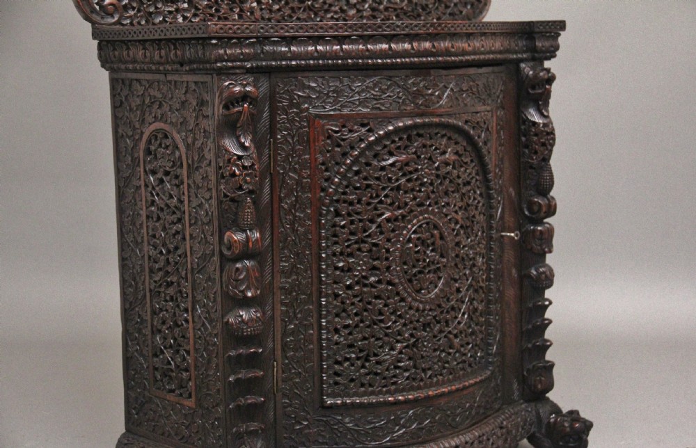 A 19th-century dark wood Anglo-Indian cabinet featuring intricate pierced floral carving, an arched panel door, and carved lion feet. View X