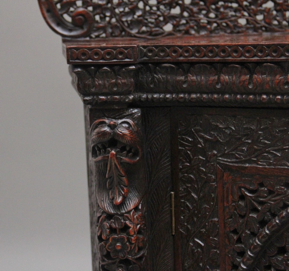A 19th-century dark wood Anglo-Indian cabinet featuring intricate pierced floral carving, an arched panel door, and carved lion feet. View XI