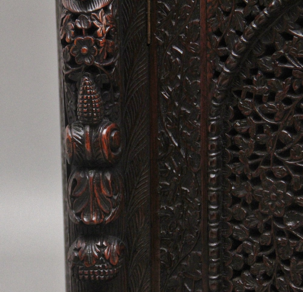 A 19th-century dark wood Anglo-Indian cabinet featuring intricate pierced floral carving, an arched panel door, and carved lion feet. View XII