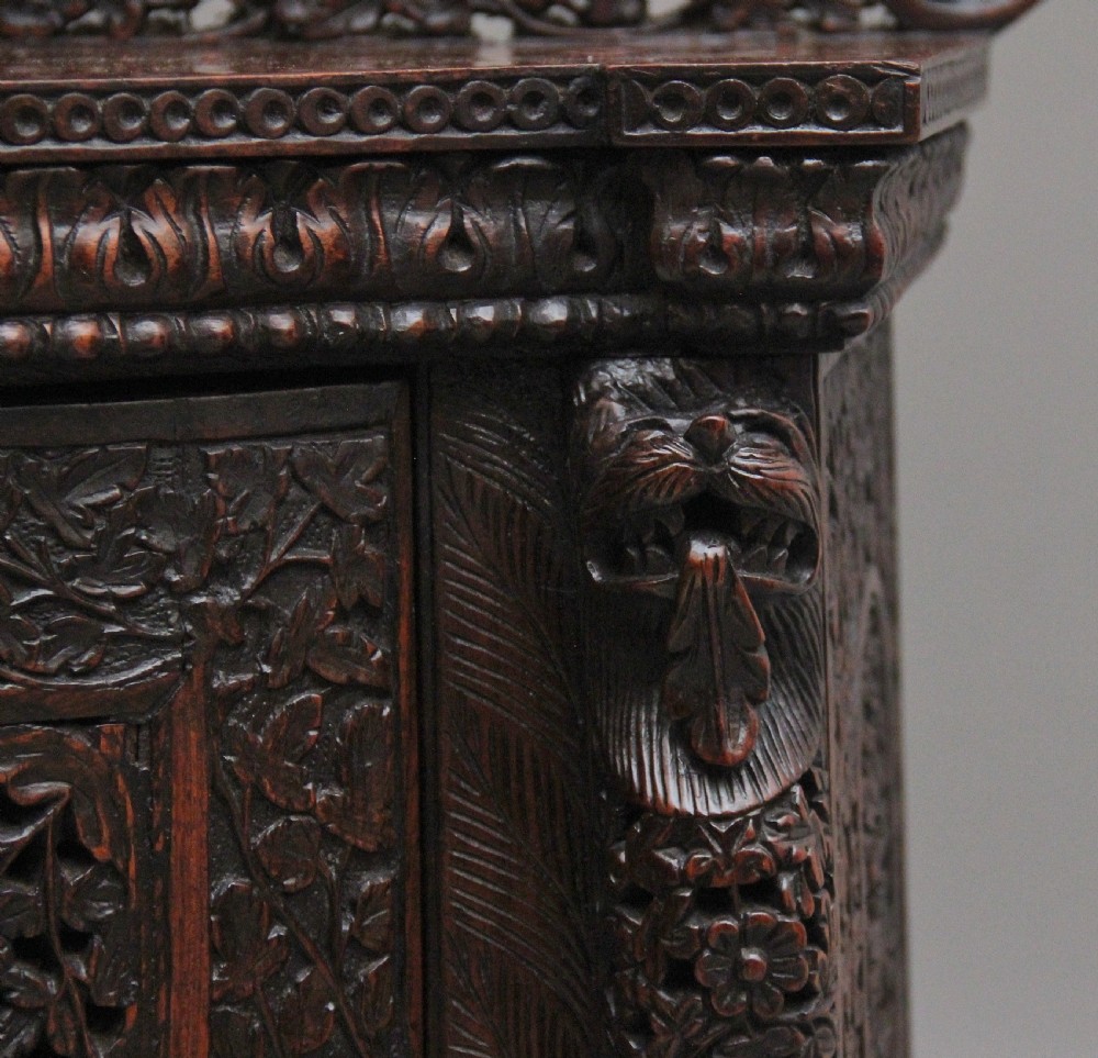 A 19th-century dark wood Anglo-Indian cabinet featuring intricate pierced floral carving, an arched panel door, and carved lion feet. View XIV