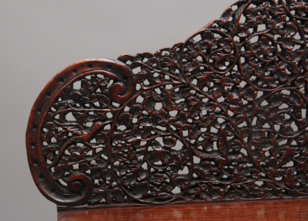 A 19th-century dark wood Anglo-Indian cabinet featuring intricate pierced floral carving, an arched panel door, and carved lion feet. View XV