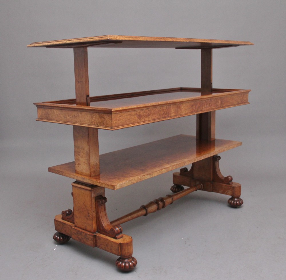An early 19th-century pollard oak dumb waiter featuring three rectangular tiered shelves supported by upright pillars and a carved trestle base with lobed feet.