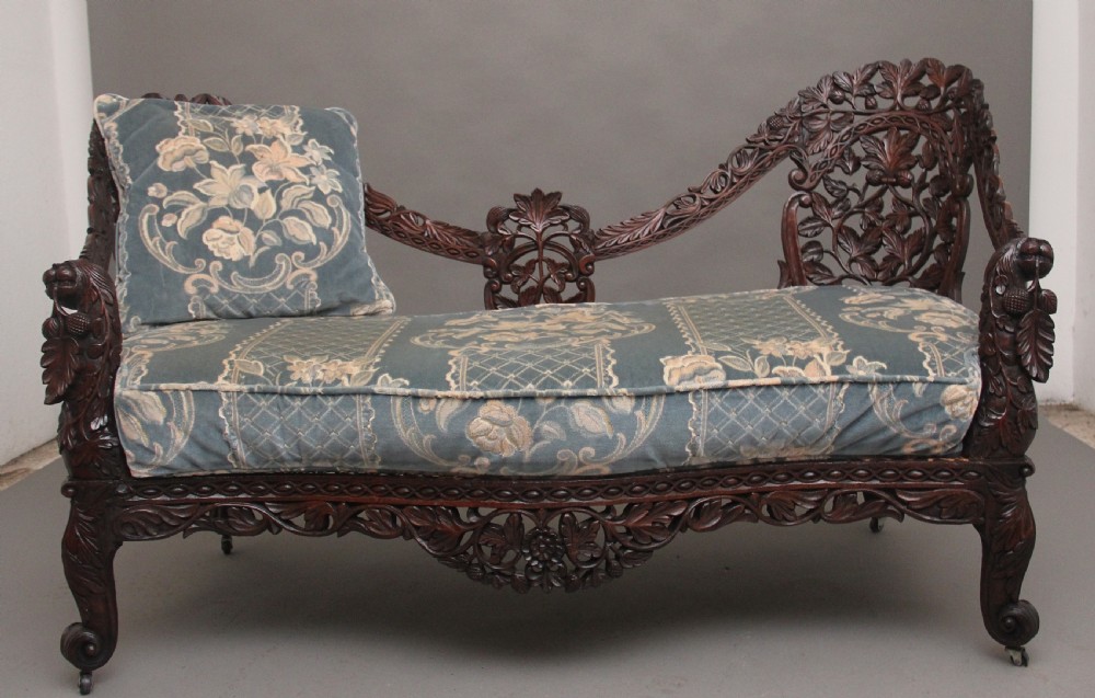 A 19th-century Anglo-Indian carved dark hardwood sofa featuring intricate foliage openwork, lion head armrests, and a patterned blue upholstered seat. View II