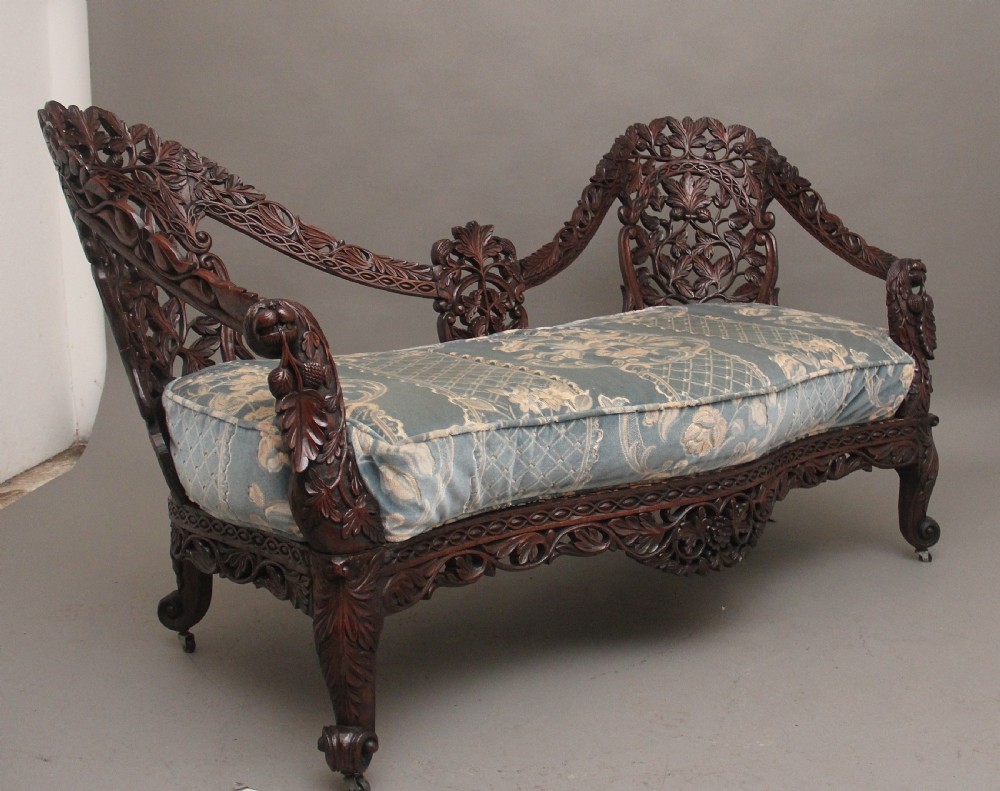A 19th-century Anglo-Indian carved dark hardwood sofa featuring intricate foliage openwork, lion head armrests, and a patterned blue upholstered seat. View III