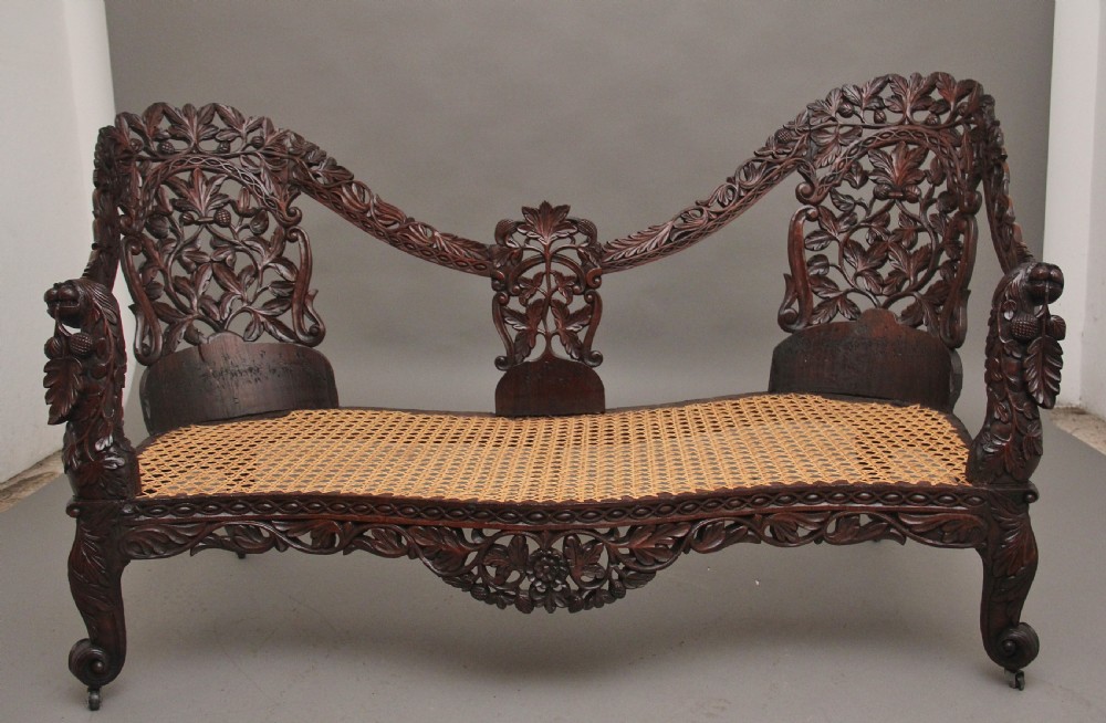 A 19th-century Anglo-Indian carved dark hardwood sofa featuring intricate foliage openwork, lion head armrests, and a patterned blue upholstered seat. View V