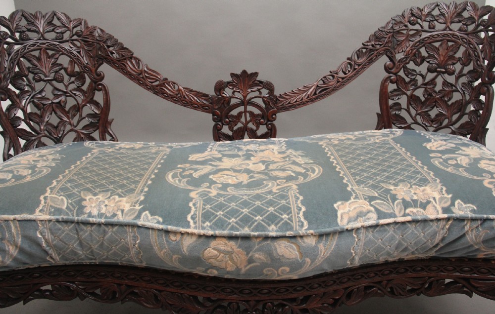 A 19th-century Anglo-Indian carved dark hardwood sofa featuring intricate foliage openwork, lion head armrests, and a patterned blue upholstered seat. View VI