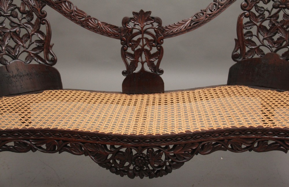 A 19th-century Anglo-Indian carved dark hardwood sofa featuring intricate foliage openwork, lion head armrests, and a patterned blue upholstered seat. View VII