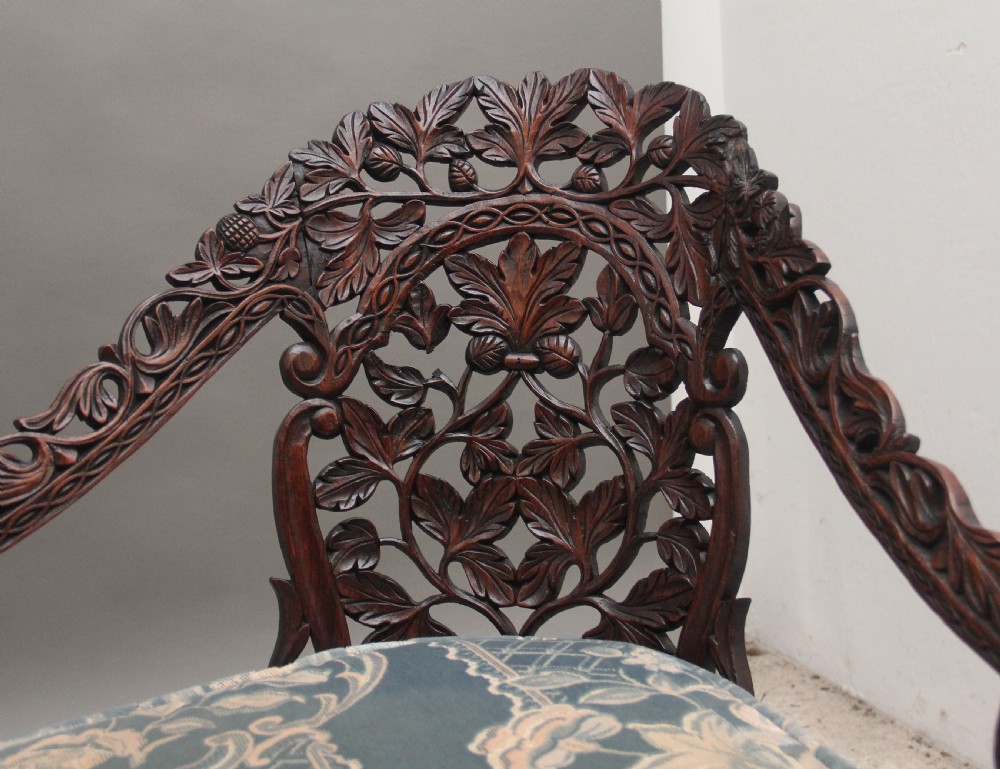 A 19th-century Anglo-Indian carved dark hardwood sofa featuring intricate foliage openwork, lion head armrests, and a patterned blue upholstered seat. View VIII
