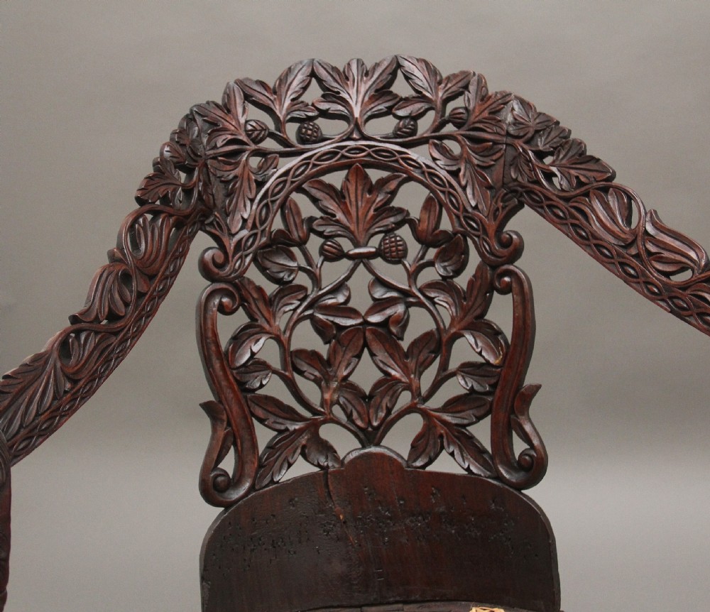 A 19th-century Anglo-Indian carved dark hardwood sofa featuring intricate foliage openwork, lion head armrests, and a patterned blue upholstered seat. View X
