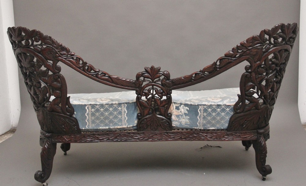A 19th-century Anglo-Indian carved dark hardwood sofa featuring intricate foliage openwork, lion head armrests, and a patterned blue upholstered seat. View XII