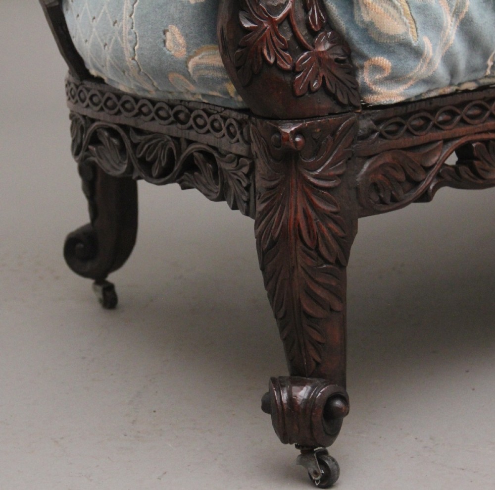 A 19th-century Anglo-Indian carved dark hardwood sofa featuring intricate foliage openwork, lion head armrests, and a patterned blue upholstered seat. View XVI