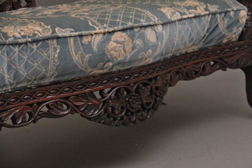 A 19th-century Anglo-Indian carved dark hardwood sofa featuring intricate foliage openwork, lion head armrests, and a patterned blue upholstered seat. View XVII