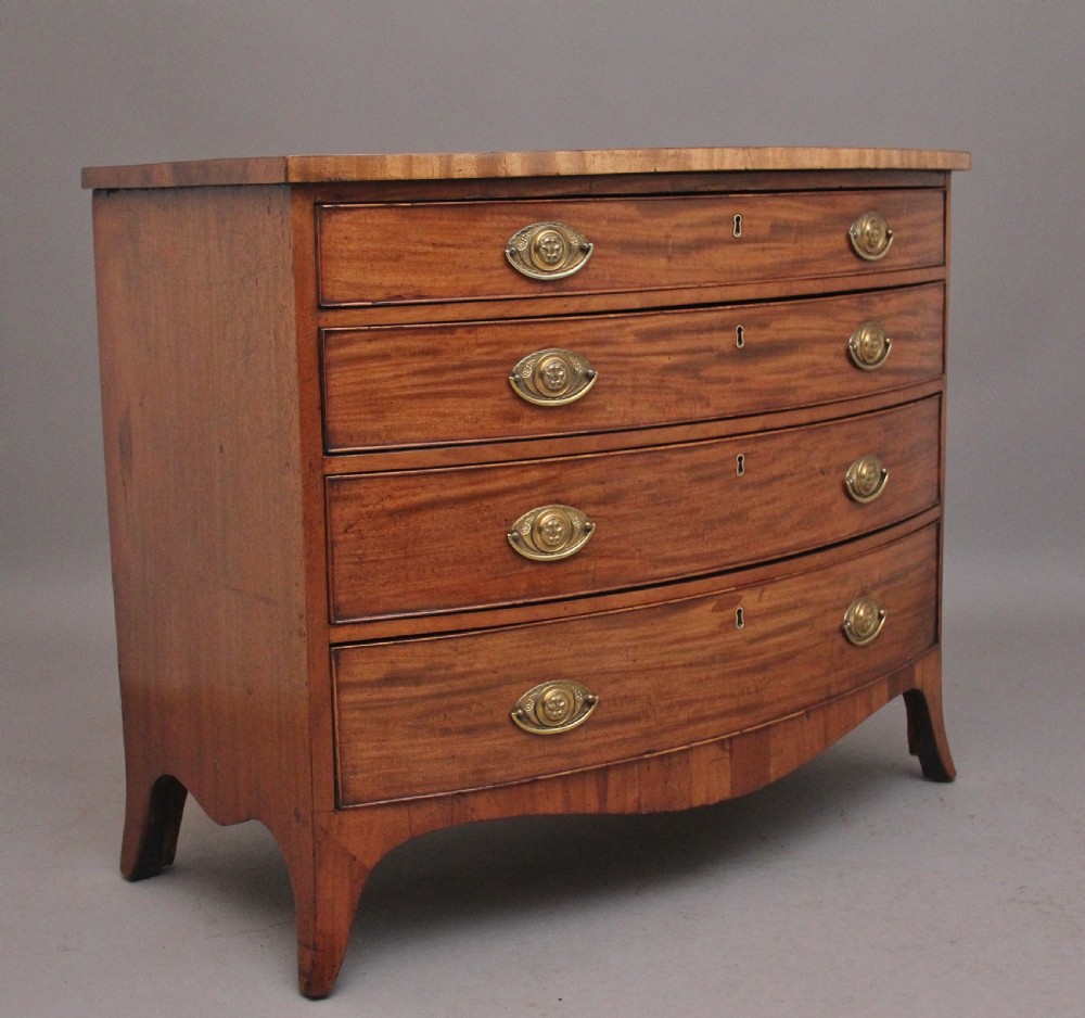 A nineteenth-century mahogany bowfront chest of drawers featuring four graduated drawers with oval brass handles and splayed feet. View II