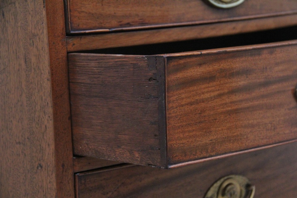 A nineteenth-century mahogany bowfront chest of drawers featuring four graduated drawers with oval brass handles and splayed feet. View V