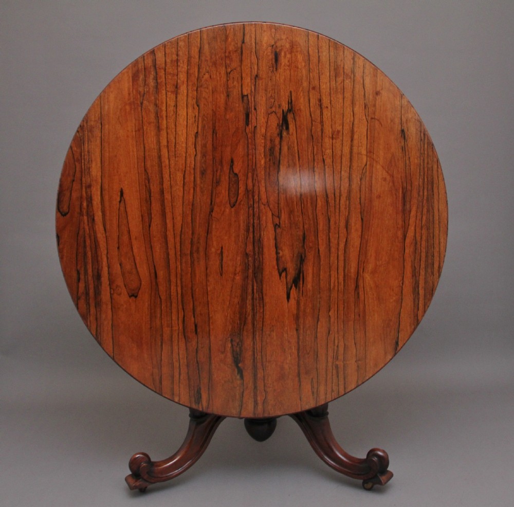 A 19th-century circular rosewood breakfast table displayed tilted upright on a carved tripod base with scroll feet. View II