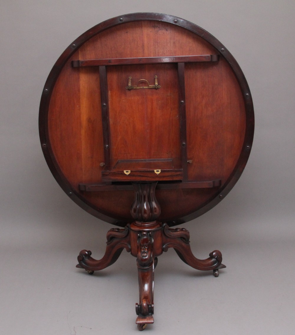 A 19th-century circular rosewood breakfast table displayed tilted upright on a carved tripod base with scroll feet. View IV