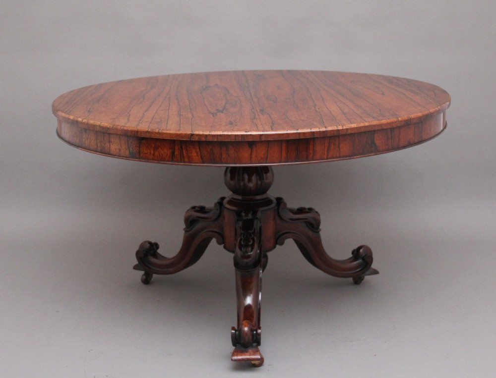 A 19th-century circular rosewood breakfast table displayed tilted upright on a carved tripod base with scroll feet. View VI