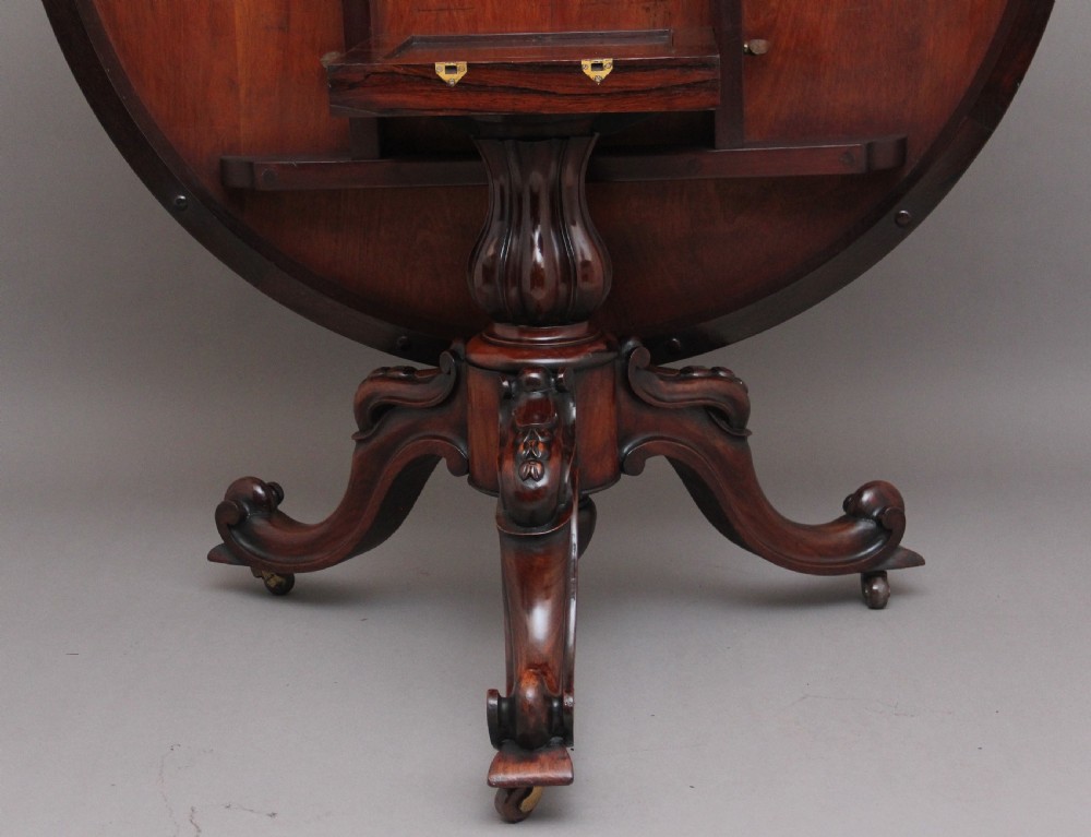 A 19th-century circular rosewood breakfast table displayed tilted upright on a carved tripod base with scroll feet. View VII