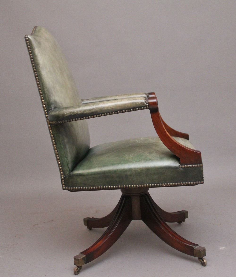 An early 20th century revolving desk chair featuring olive green leather upholstery with brass studding trim and carved mahogany armrests on a four-star base. View III