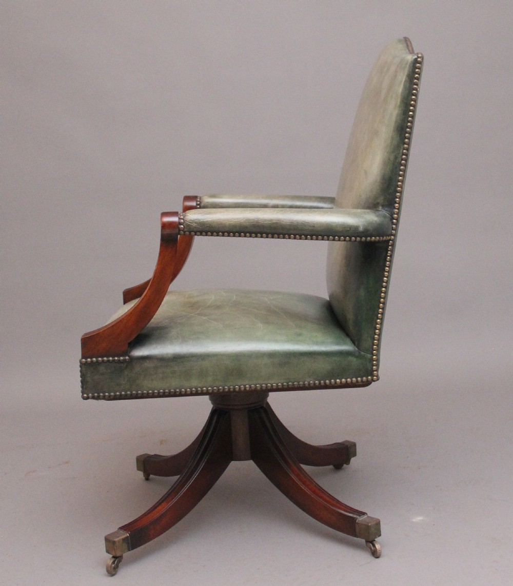 An early 20th century revolving desk chair featuring olive green leather upholstery with brass studding trim and carved mahogany armrests on a four-star base. View VI