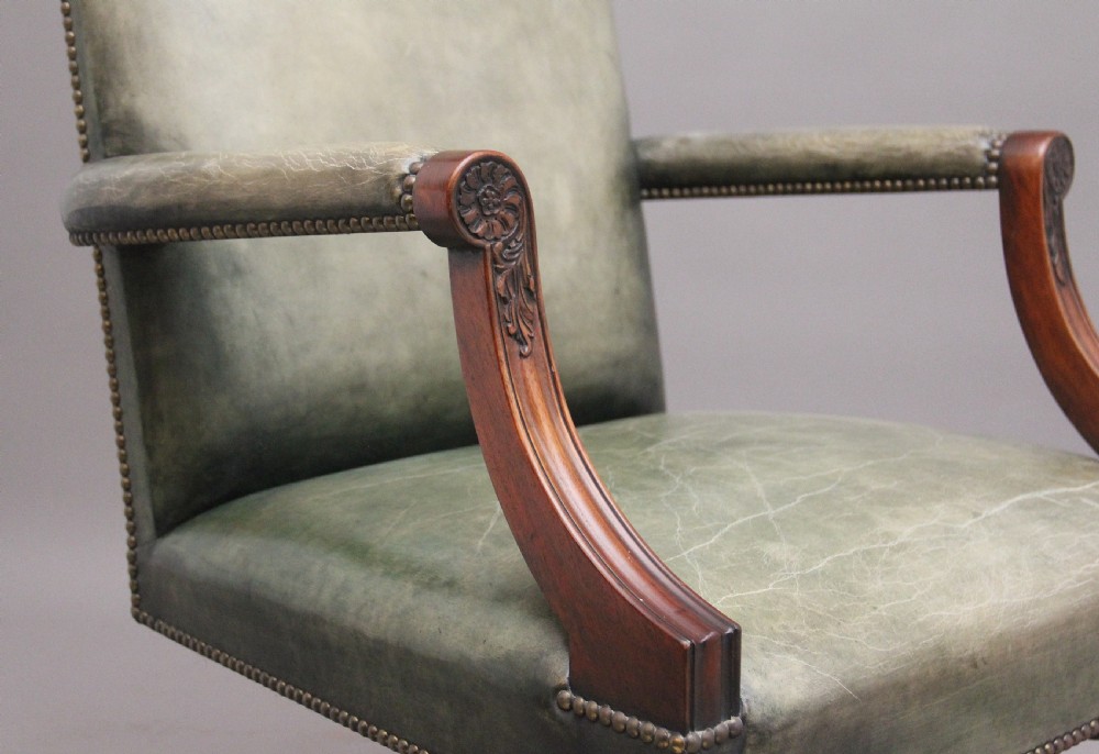 An early 20th century revolving desk chair featuring olive green leather upholstery with brass studding trim and carved mahogany armrests on a four-star base. View VIII