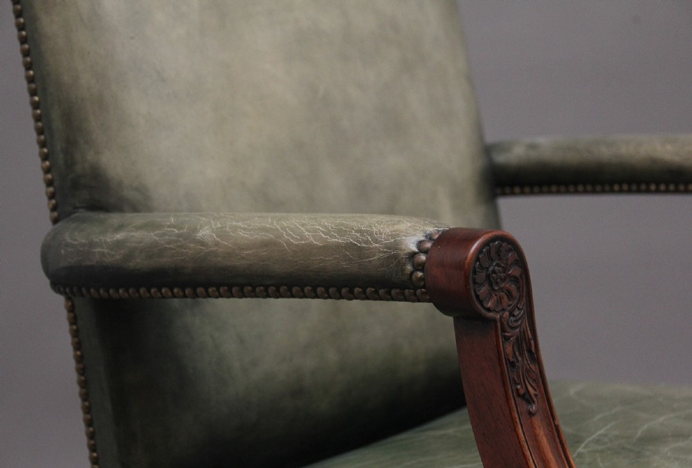 An early 20th century revolving desk chair featuring olive green leather upholstery with brass studding trim and carved mahogany armrests on a four-star base. View XI