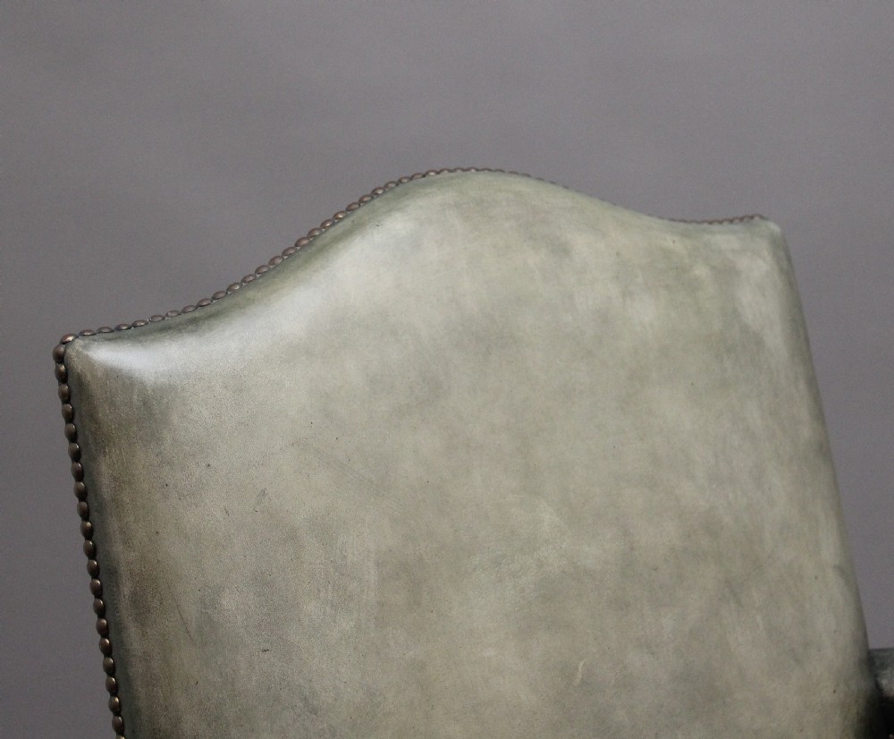 An early 20th century revolving desk chair featuring olive green leather upholstery with brass studding trim and carved mahogany armrests on a four-star base. View XII