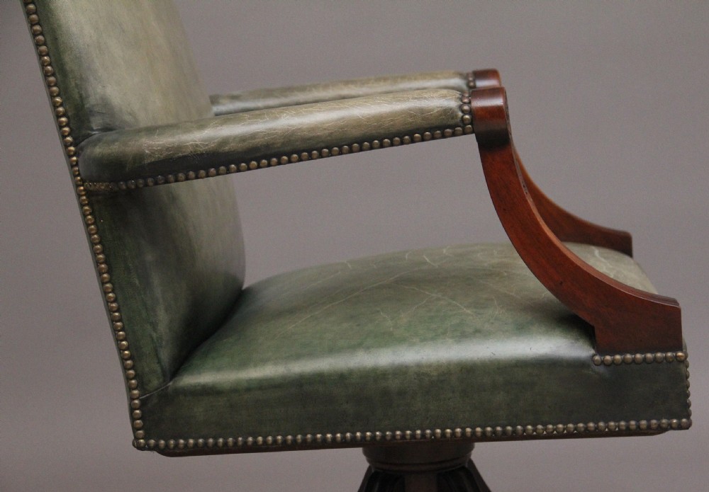 An early 20th century revolving desk chair featuring olive green leather upholstery with brass studding trim and carved mahogany armrests on a four-star base. View XIII