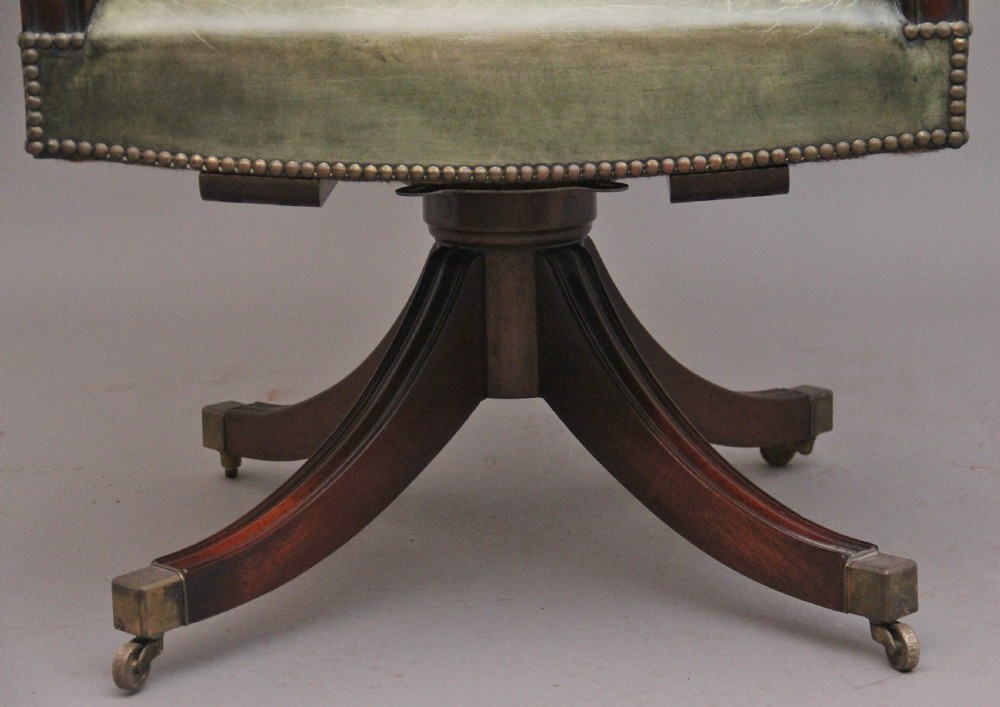 An early 20th century revolving desk chair featuring olive green leather upholstery with brass studding trim and carved mahogany armrests on a four-star base. View XIV