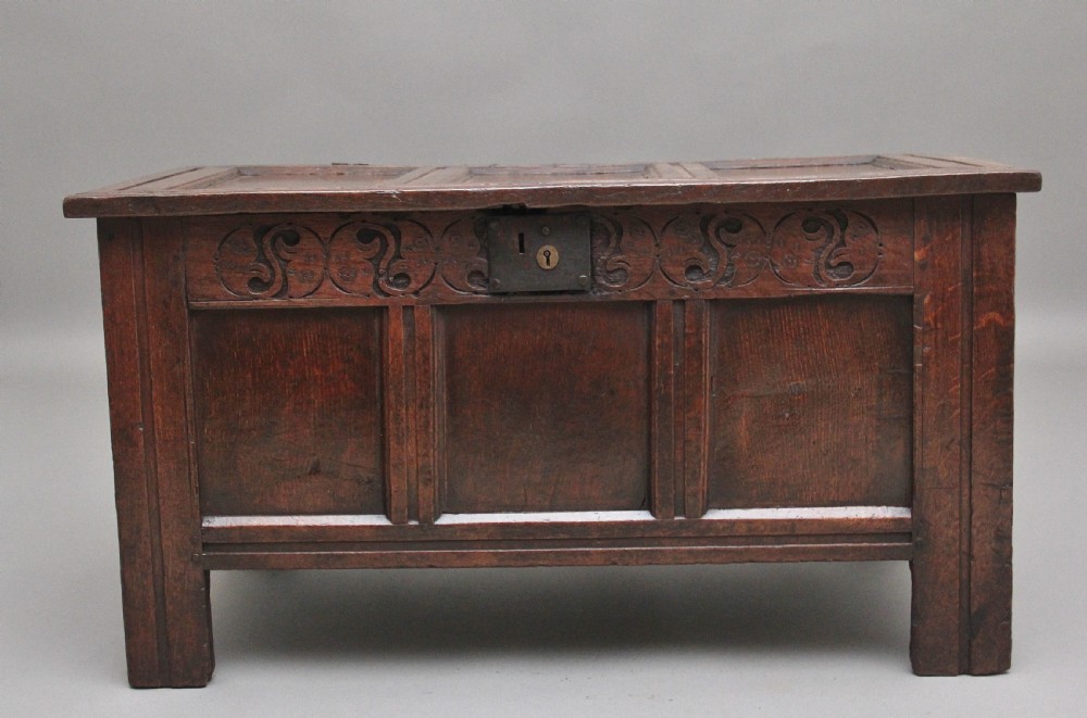An early 18th-century dark oak coffer featuring three sunken front panels, a hand-carved frieze, and a central iron lock plate.