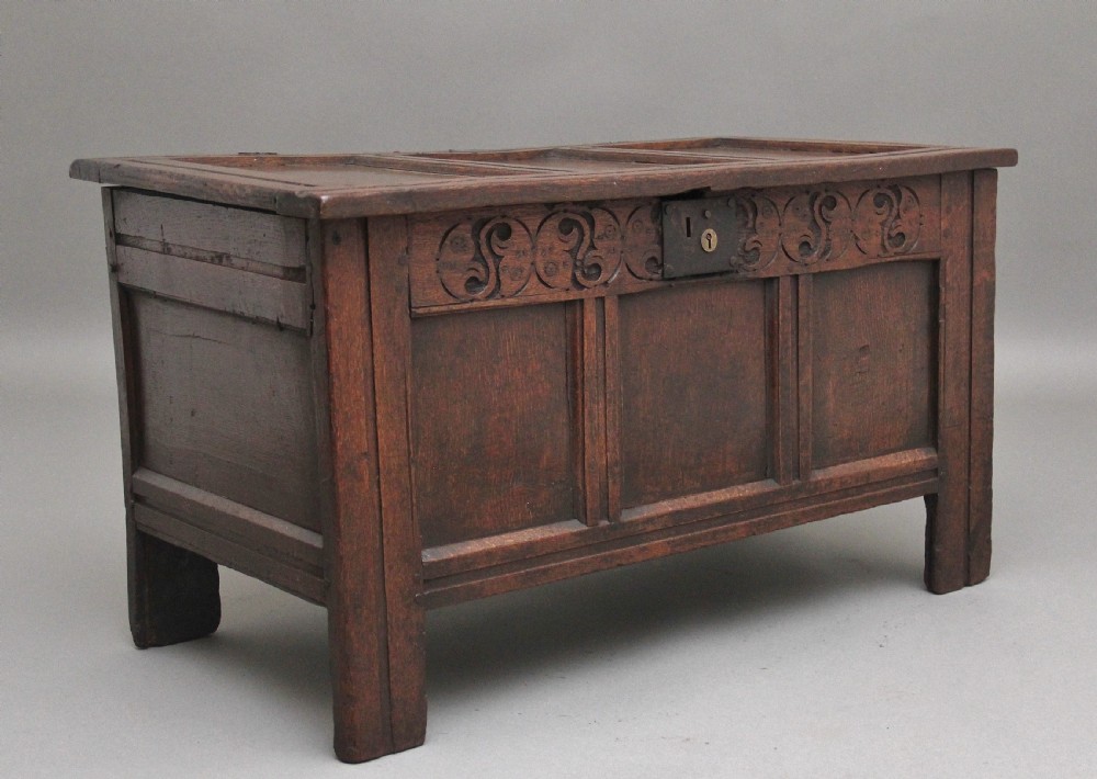 An early 18th-century dark oak coffer featuring three sunken front panels, a hand-carved frieze, and a central iron lock plate. View II