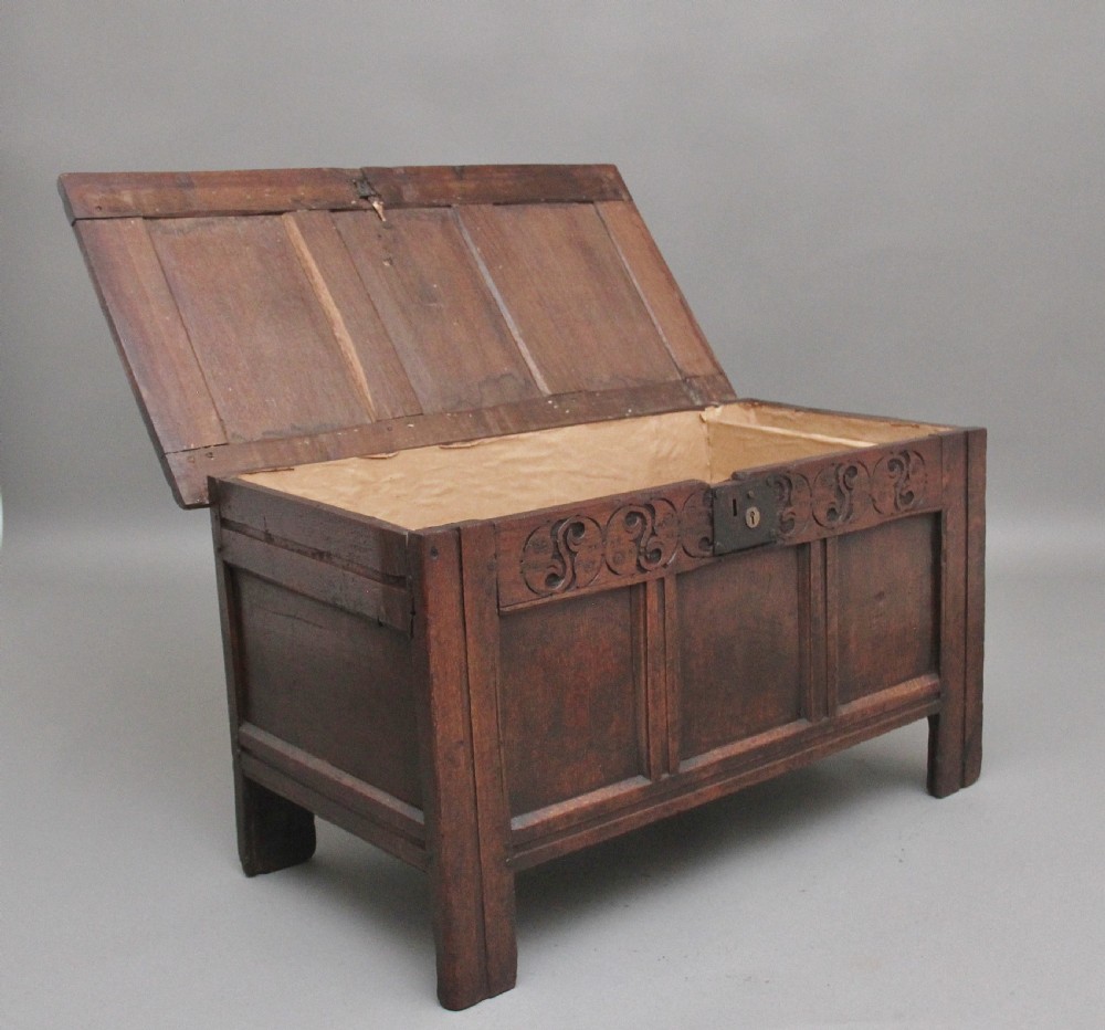 An early 18th-century dark oak coffer featuring three sunken front panels, a hand-carved frieze, and a central iron lock plate. View III