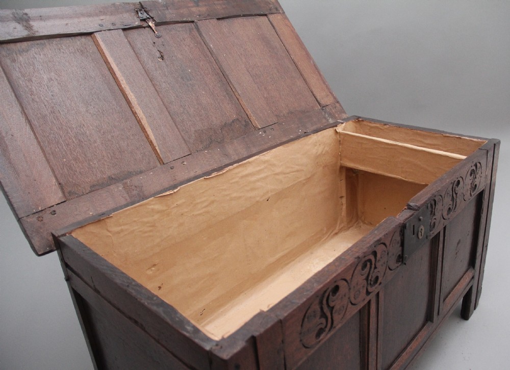 An early 18th-century dark oak coffer featuring three sunken front panels, a hand-carved frieze, and a central iron lock plate. View V