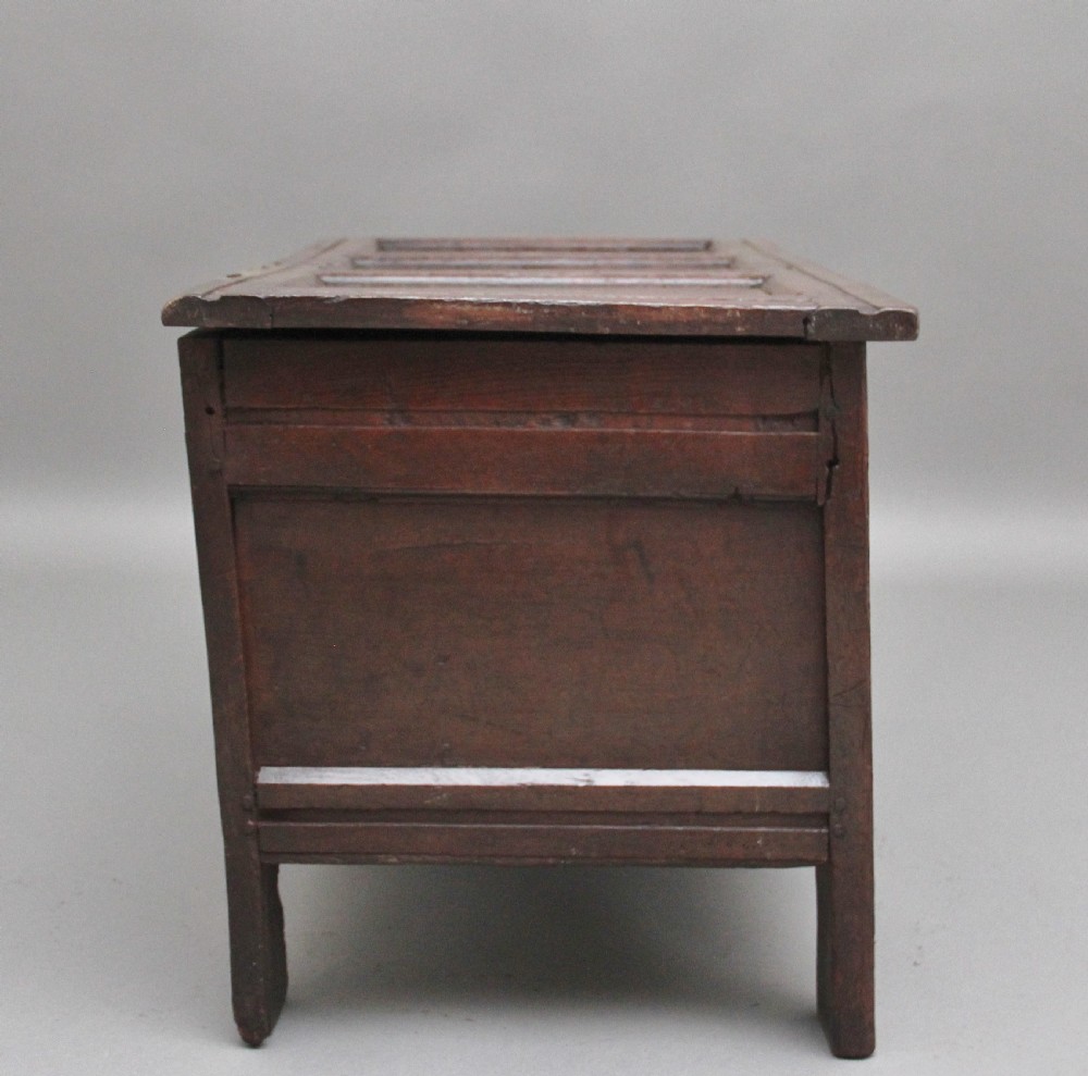 An early 18th-century dark oak coffer featuring three sunken front panels, a hand-carved frieze, and a central iron lock plate. View VI