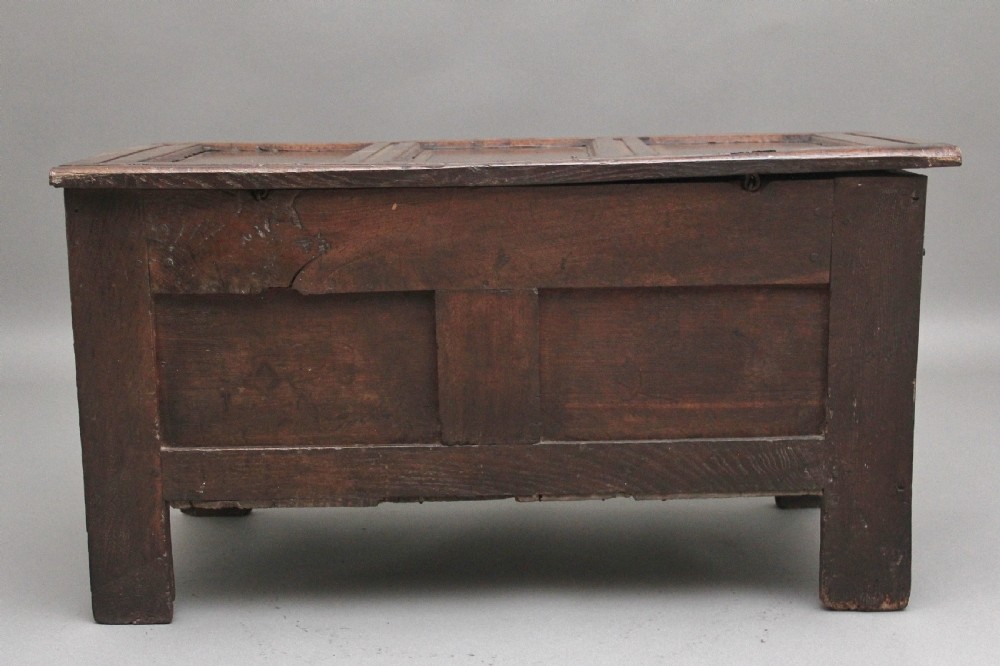 An early 18th-century dark oak coffer featuring three sunken front panels, a hand-carved frieze, and a central iron lock plate. View VII