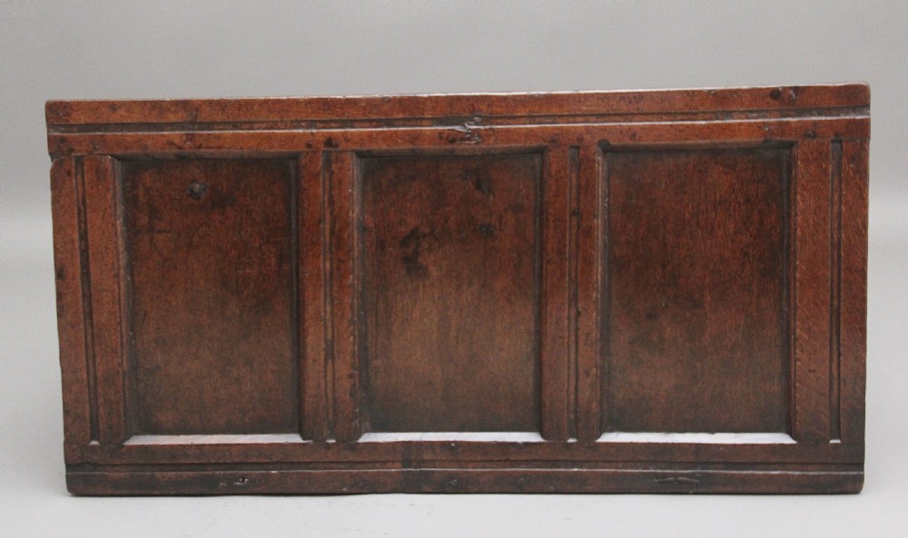 An early 18th-century dark oak coffer featuring three sunken front panels, a hand-carved frieze, and a central iron lock plate. View VIII