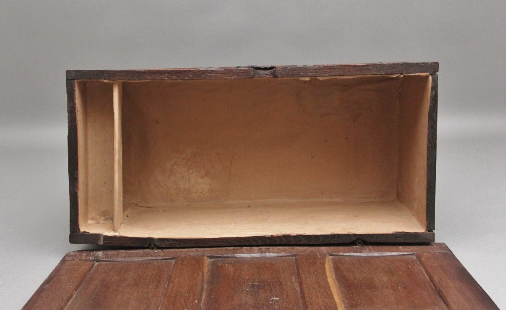 An early 18th-century dark oak coffer featuring three sunken front panels, a hand-carved frieze, and a central iron lock plate. View IX